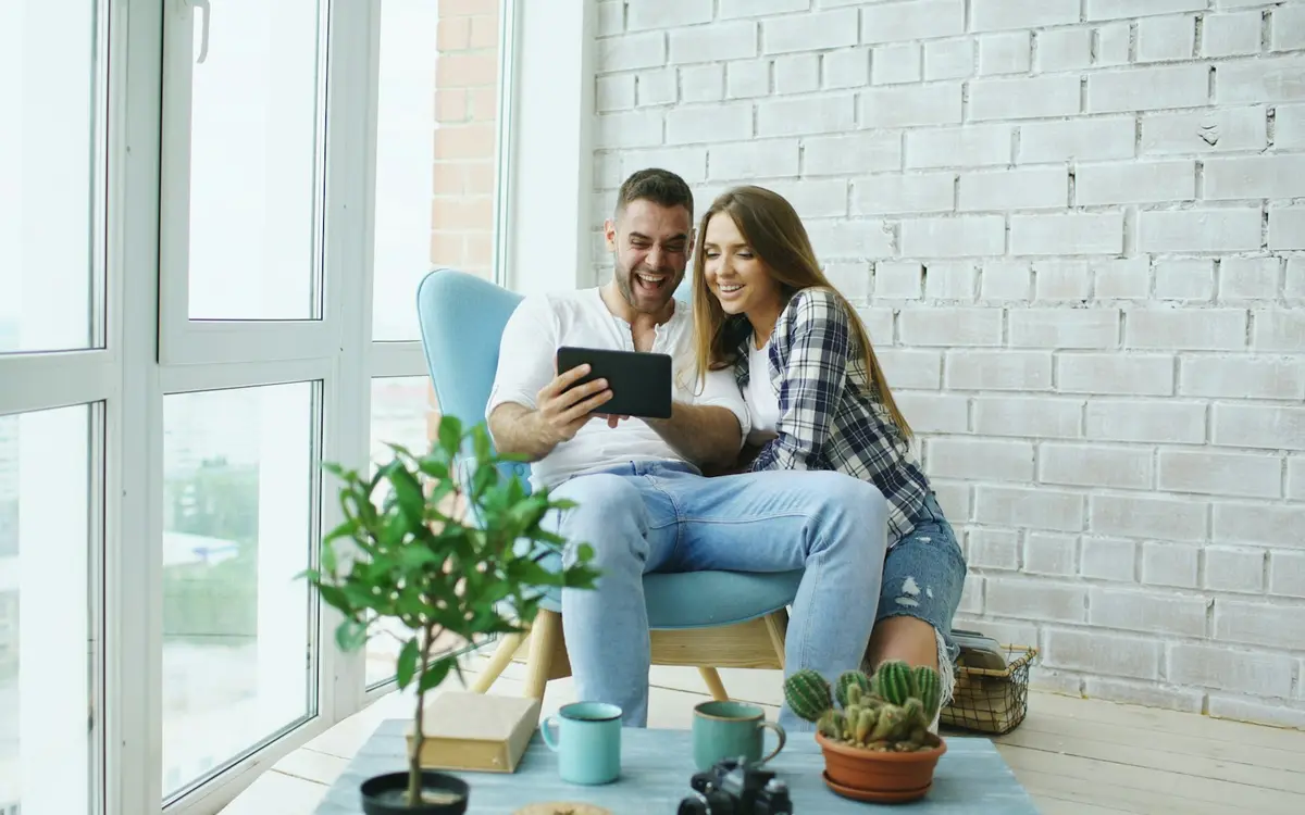 A couple sitting together in an armchair, smiling at a tablet