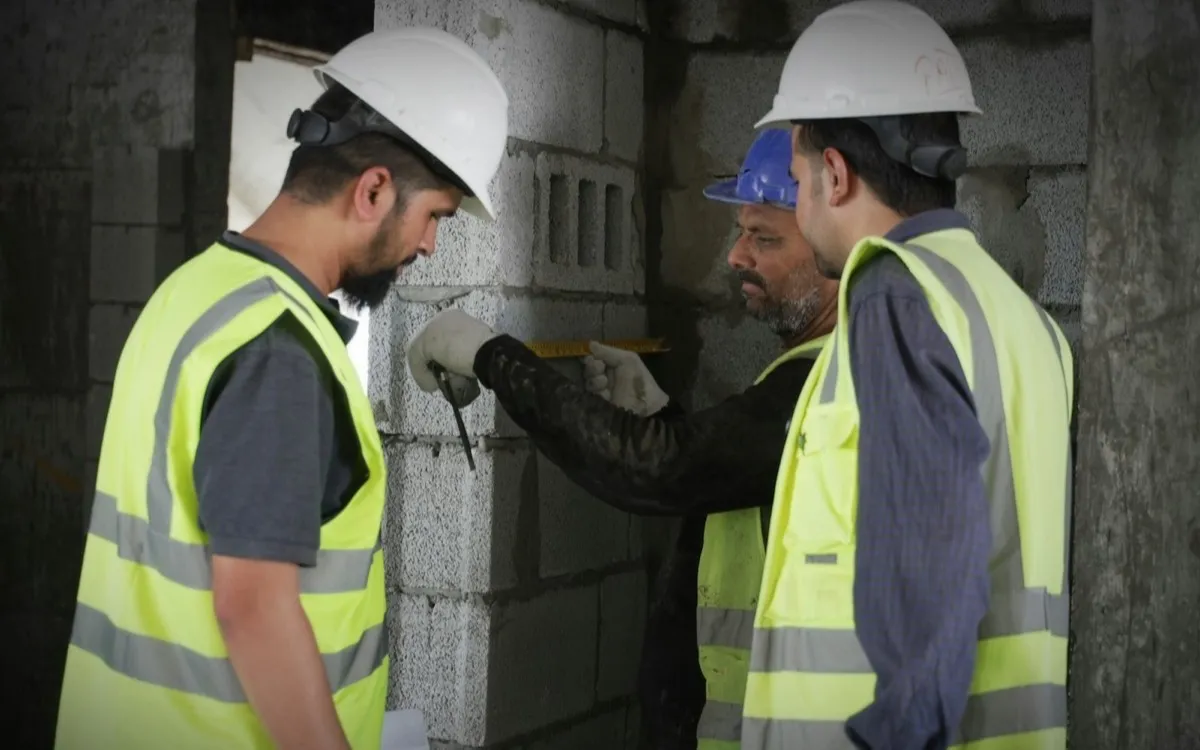 Construction workers in hard hats and hi-vis vests measuring block work on site
